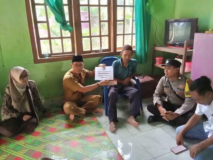 Serahkan BLT DD Kepala Desa Tanjung Baru, Hendra Oswari didampingi perangkat desa dan anggata polisi menyerahkan dana BLT DD kepada salah seorang warga desa setempat, Senin 5 April 2025.(Foto HB/Kif)