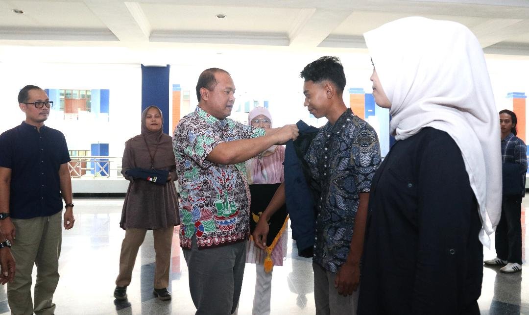 Rektor Unib, Indra Cahyadinata memasangkan jaket kepada salah seorang mahasiswa yang akan melaksanakan KKN di daerah bencana banjir Sumbar pada acara pelepasan pemberangkatan di kampus Unib, Rabu 17 Desember 2024.(Foto/Ist)